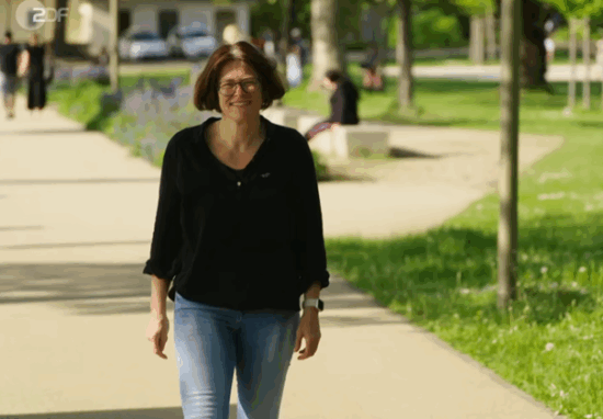Eine Frau mit dunklen Haaren, einer Brille, einemn schwarzen Hemd und blauer Jeans