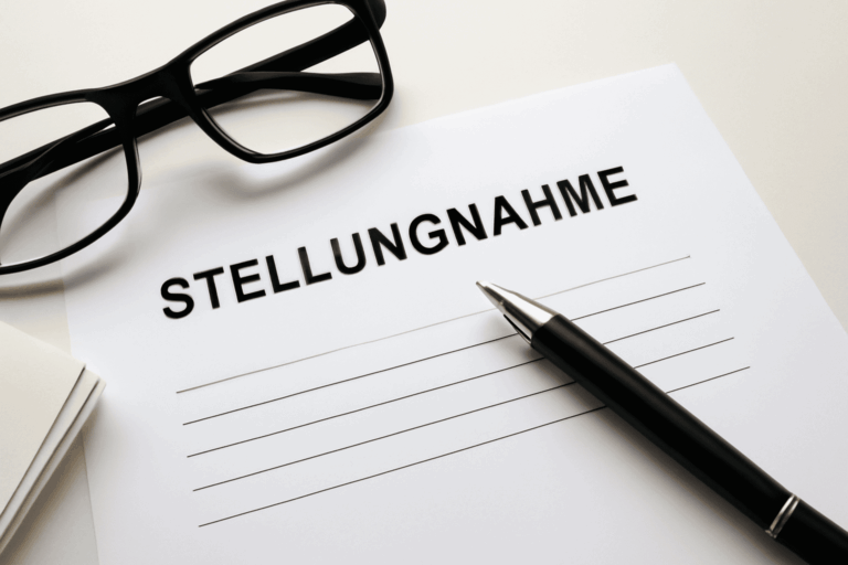 Ein weißes Blatt Papier auf dem Stellungnahme steht und daneben liegen ein Kugelschreiber und eine Brille