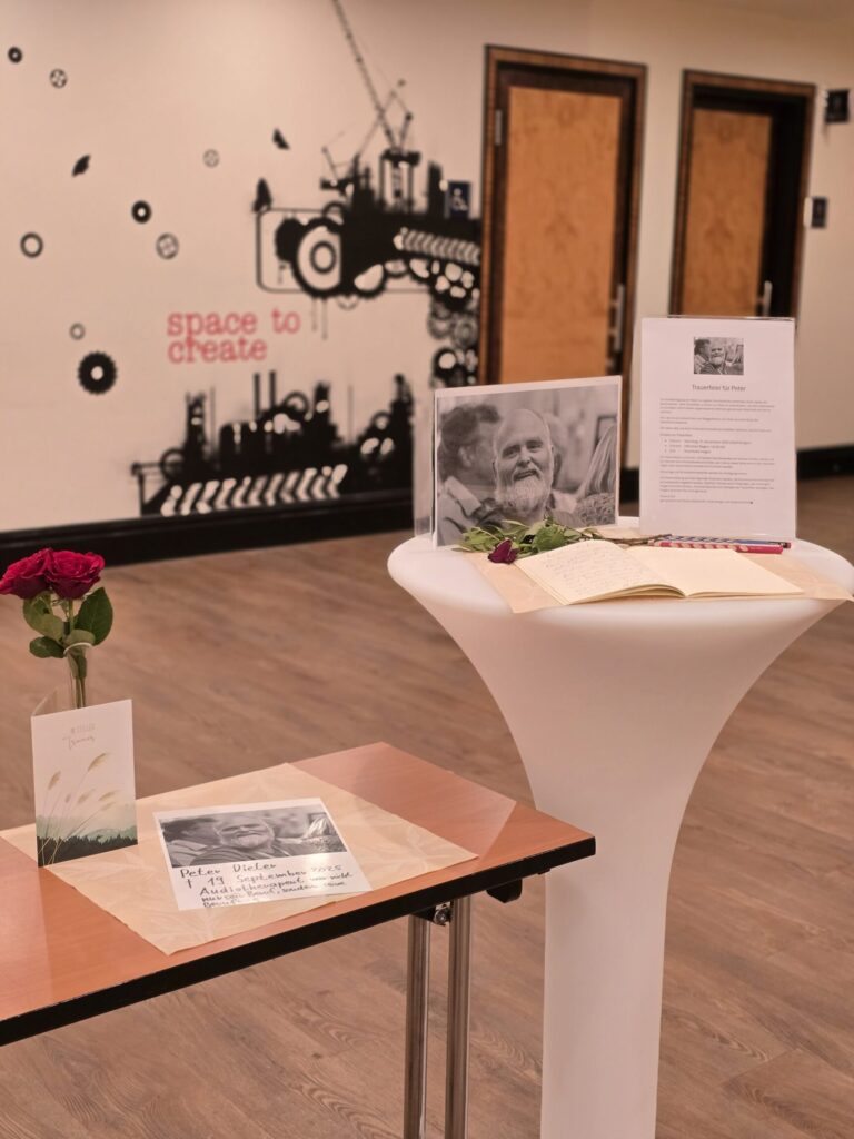 Stehtisch mit offenem Kondolenzbuch, Stift und Foto in s/w und einer roten Rose.