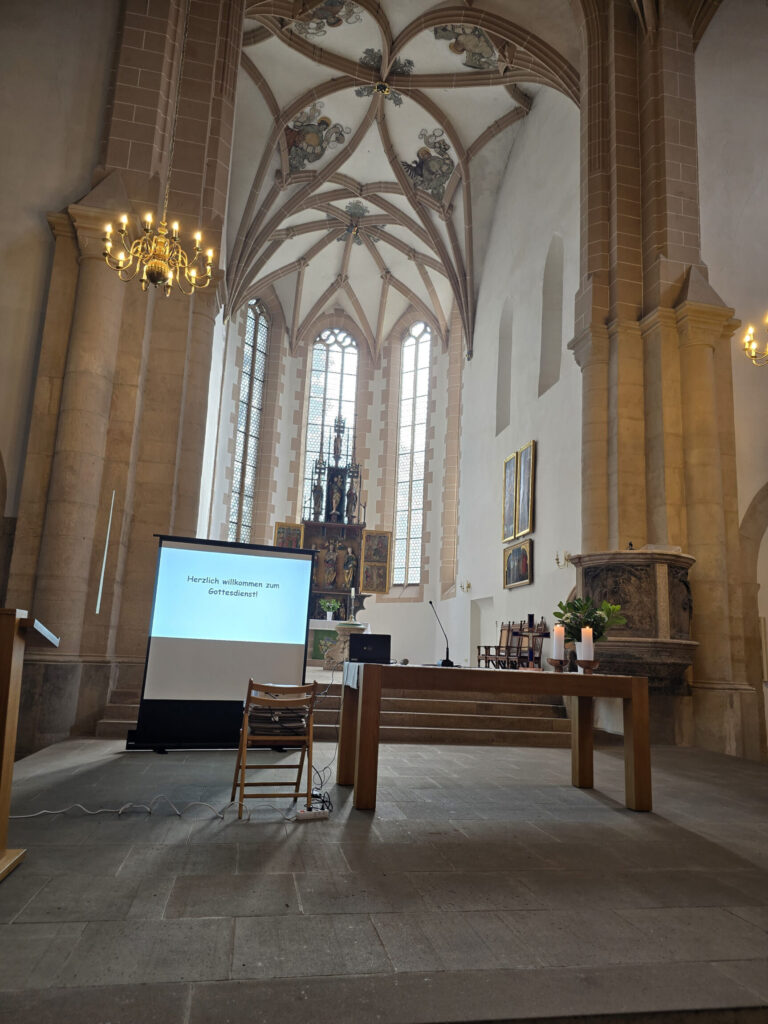 Innenraum einer Kirche mit gotischem Gewölbe, Altar, Kerzen, Stuhl und Leinwand.