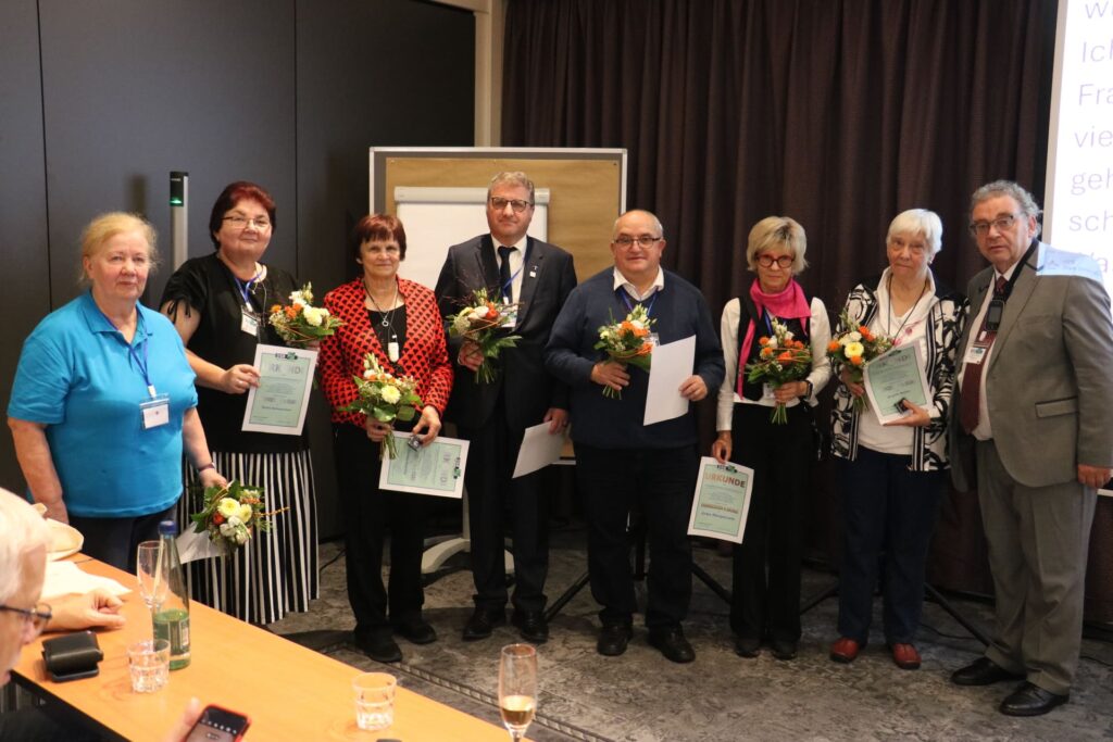 Gruppe von 8 Personen steht nebeneinander, einige halten Urkunden und Blumensträuße in den Händen.