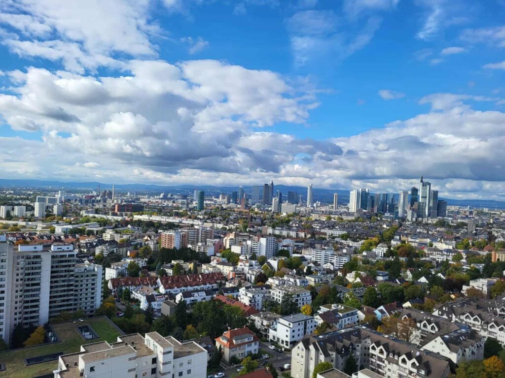 Stadtpanorama mit Wohnhäusern im Vordergrund und Hochhäusern am Horizont unter bewölktem Himmel.