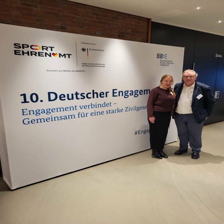 Zwei Personen stehen vor einer großen weißen Wand mit der Aufschrift '10. Deutscher Engagementtag Engagement verbindet – Gemeinsam für eine starke Zivilgesellschaft'.