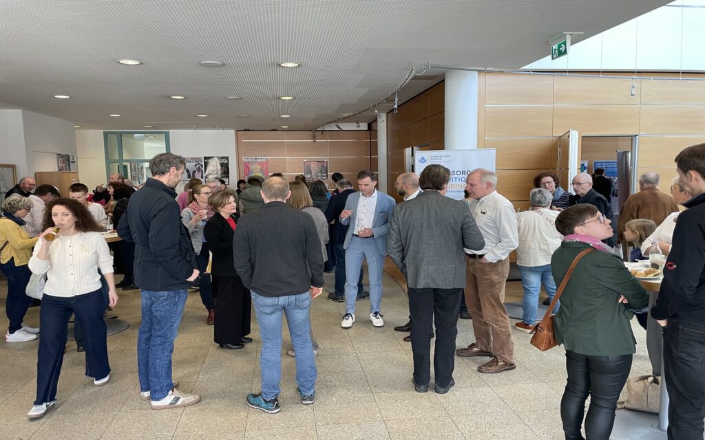 Gruppe von Menschen in einem hellen Raum mit Holzverkleidung, die sich unterhalten und Getränke halten.