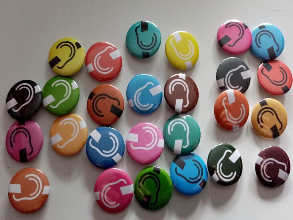 Mehrere bunte runde Buttons mit weißem durchgestrichenem weißen Ohr in verschiedenen Farben auf hellem Untergrund verteilt.