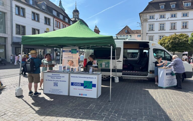 Zelt mit Informationsständen des Deutschen Schwerhörigenbunds auf einem Platz vor historischen Gebäuden.