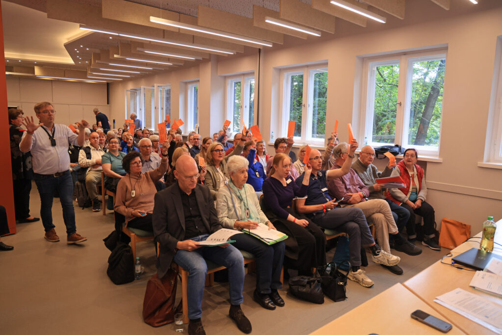 Gruppe von Menschen in einem hellen Raum hebt orangefarbene Karten bei einer Abstimmung.